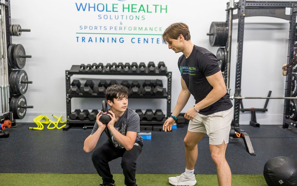 Performance coach teaching a young athlete a goblet squat in the WHS training center