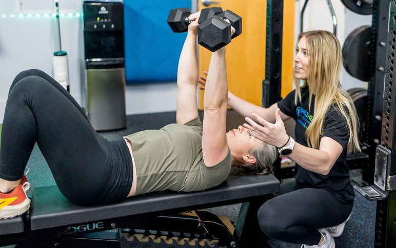 A client pressing dumbbells with support at Whole Health Solutions
