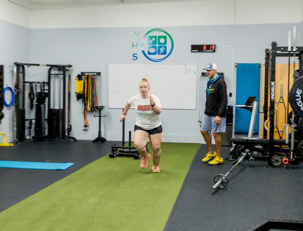 Client training on the turf while her coach watches in the WHS training center
